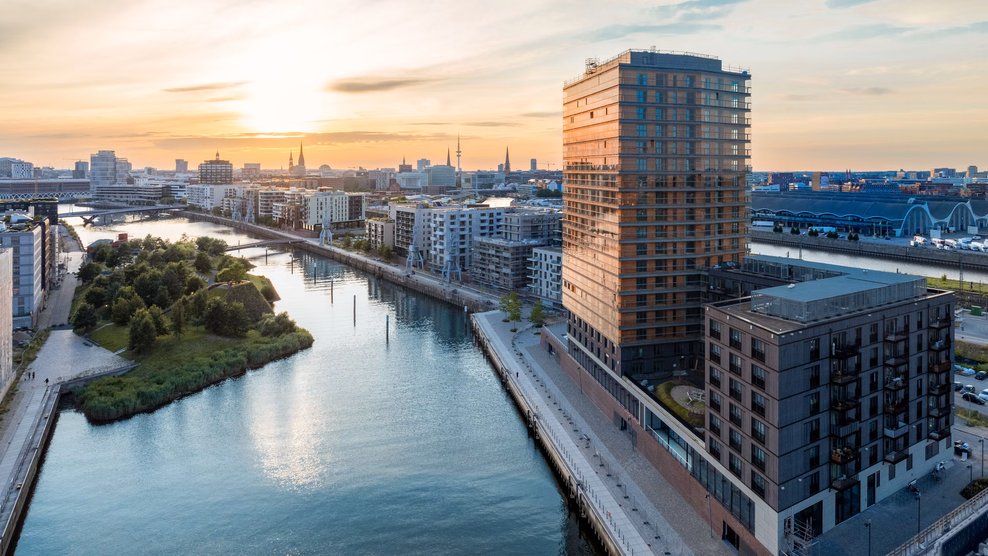 Stadtquartier am Fluss mit hohen Wohngebäuden und Sonnenuntergang im Hintergrund