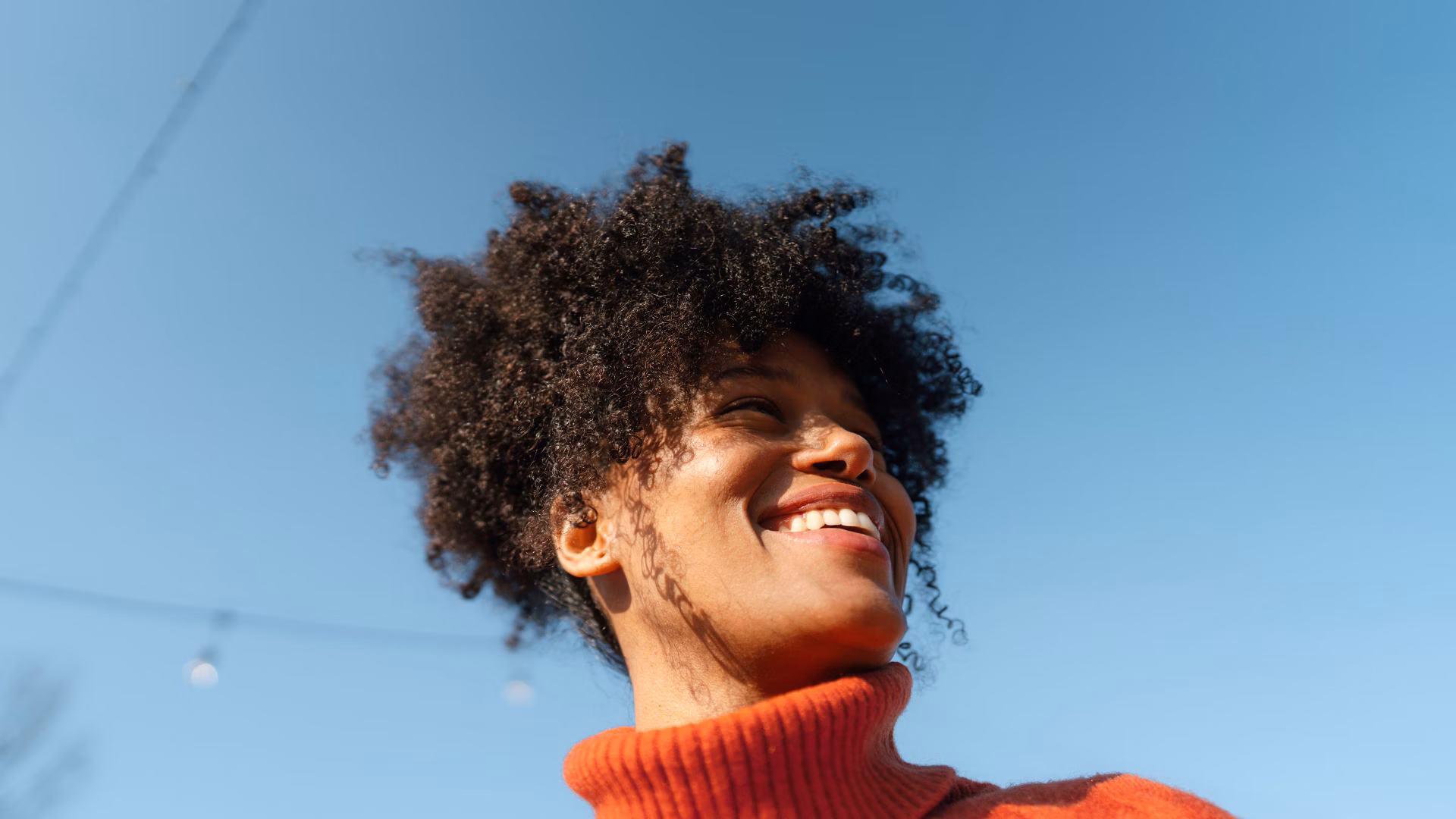 Smiling person in a red roll-neck jumper against a blue sky