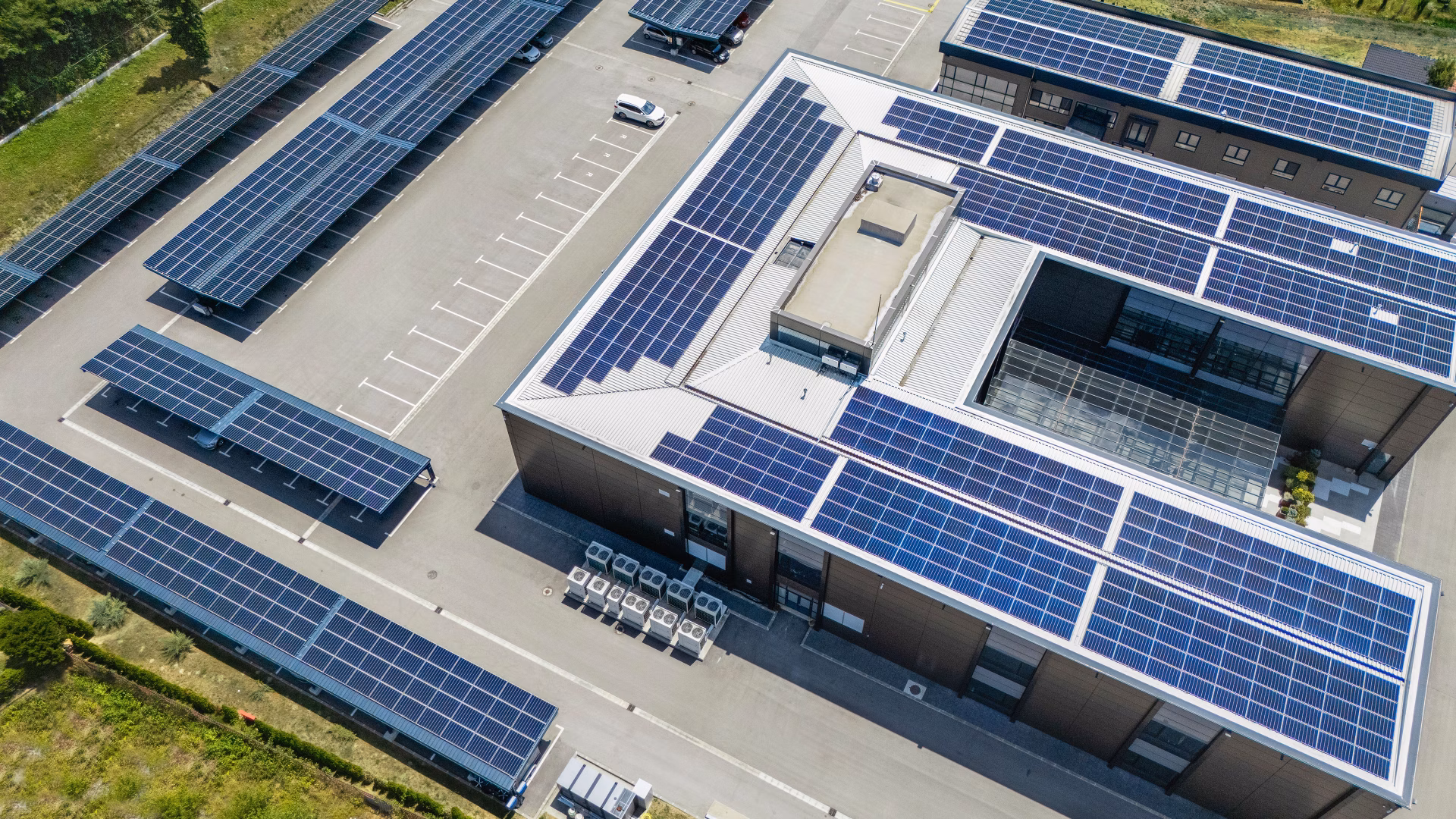 Gewerbegebäude mit grossflächigen Solaranlagen auf Dächern und Parkplätzen aus der Vogelperspektive