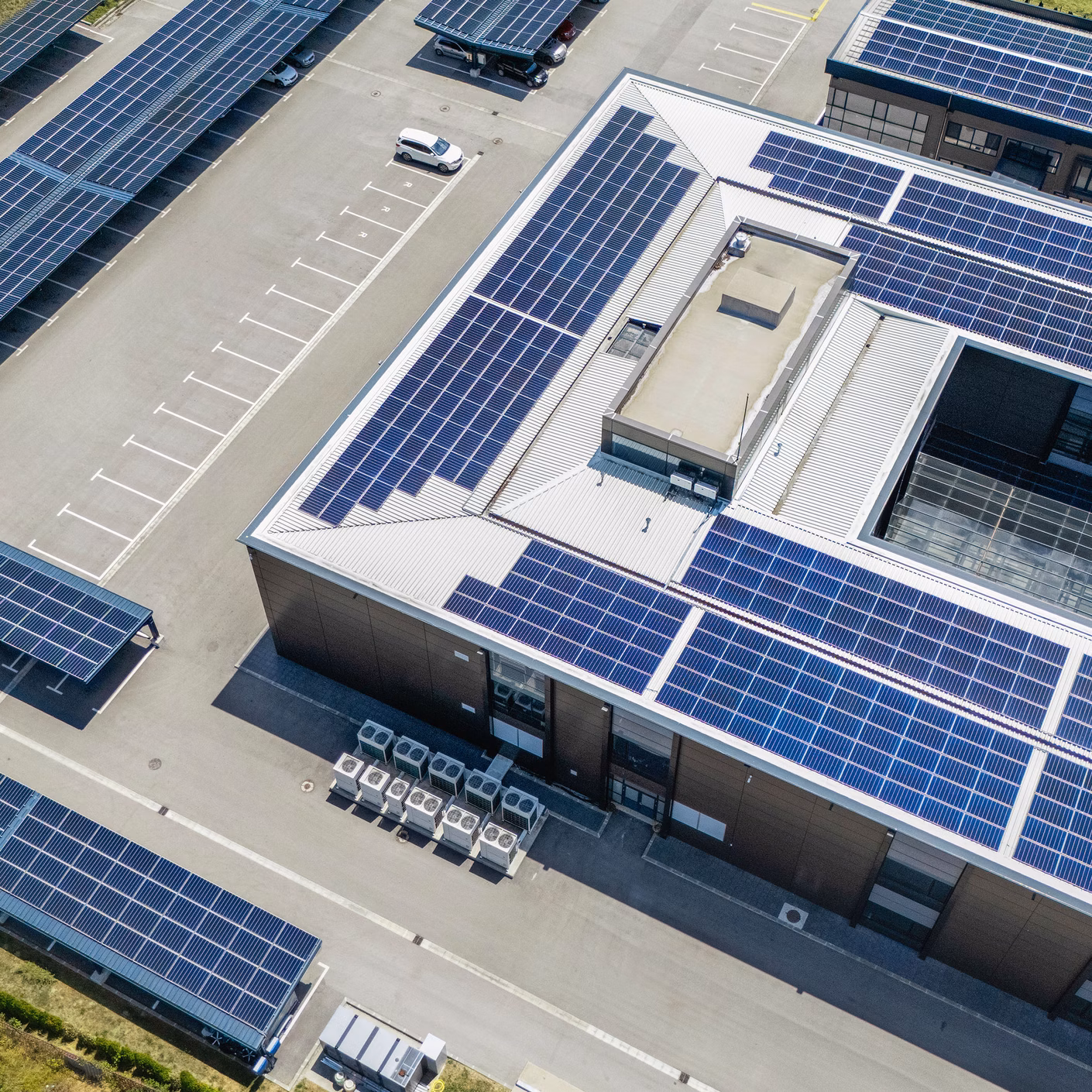 Gewerbegebäude mit grossflächigen Solaranlagen auf Dächern und Parkplätzen aus der Vogelperspektive