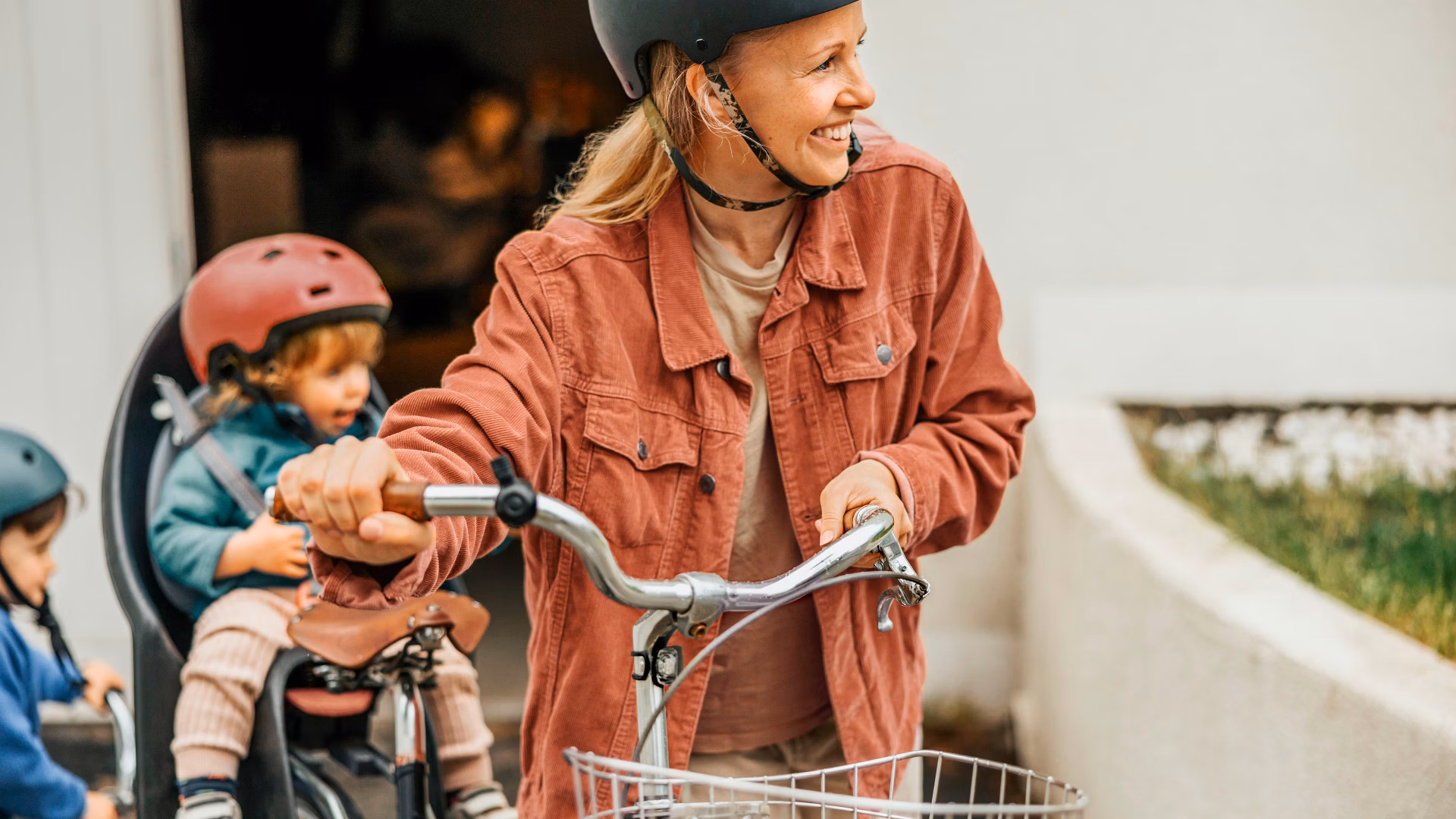 Frau mit Helm auf einem Velo, hinter ihr sitzen zwei Kinder auf einem Lastenvelo.