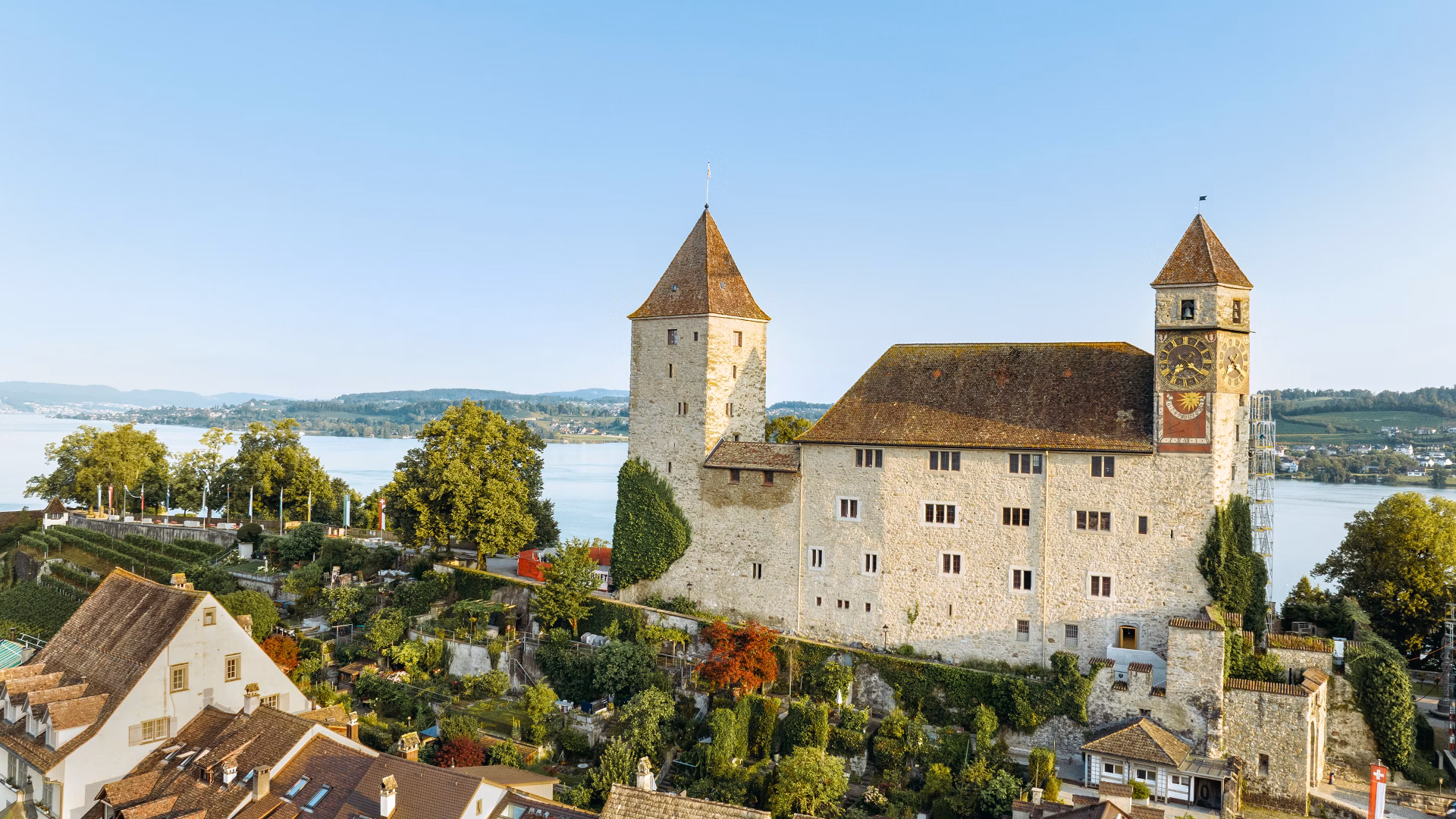 Historisches Schloss auf einem Hügel mit umliegenden Häusern und See im Hintergrund