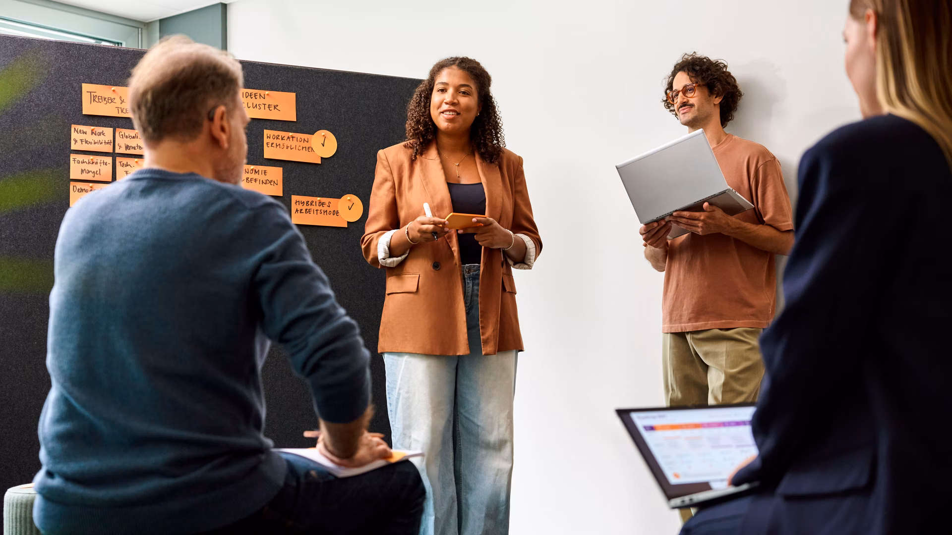Situation d’atelier avec quatre personnes, des notes sur flipchart et un ordinateur portable dans une salle de réunion lumineuse
