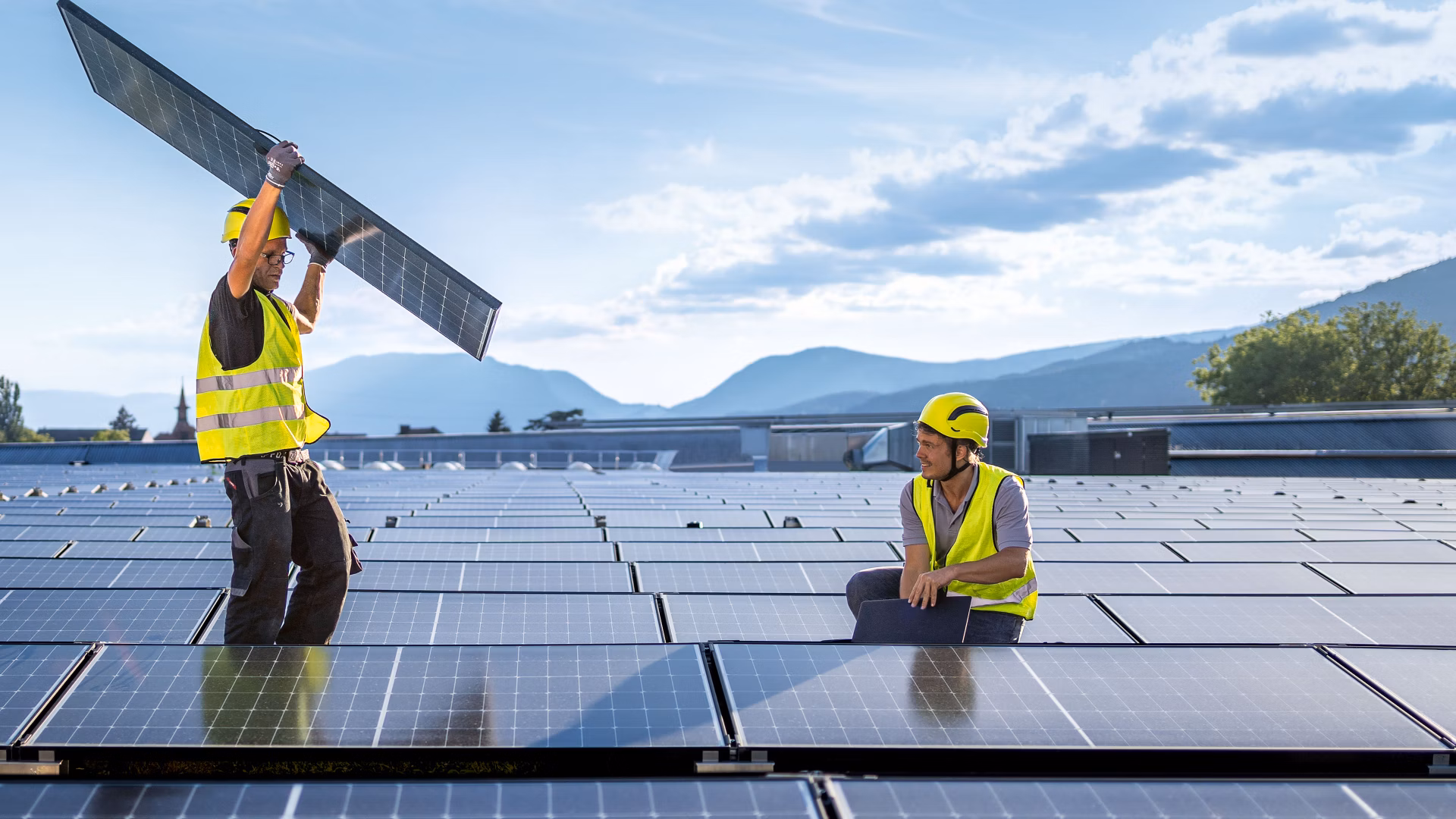 Zwei Arbeiter in Warnwesten montieren Solarpanels auf einem Dach.
