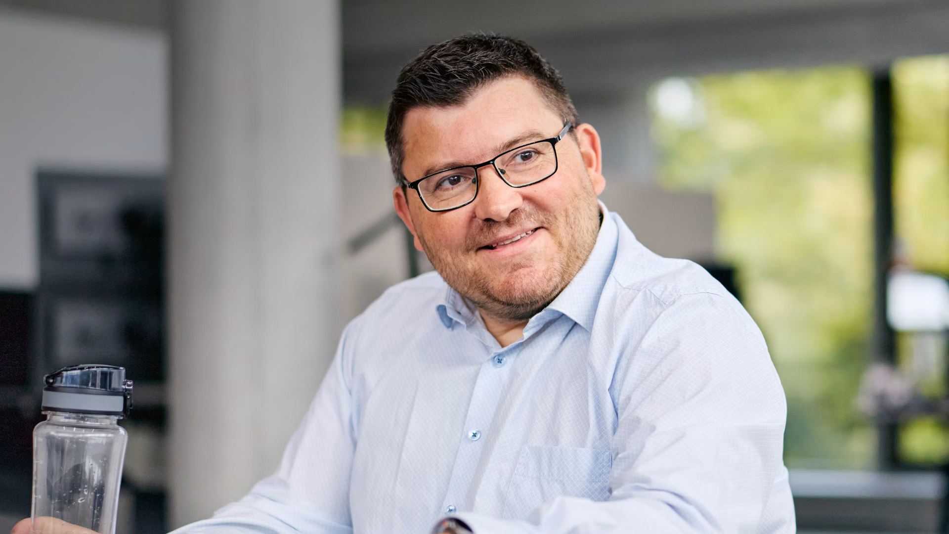 Mann mit Brille und hellem Hemd sitzt an einem Tisch in einem Büro.