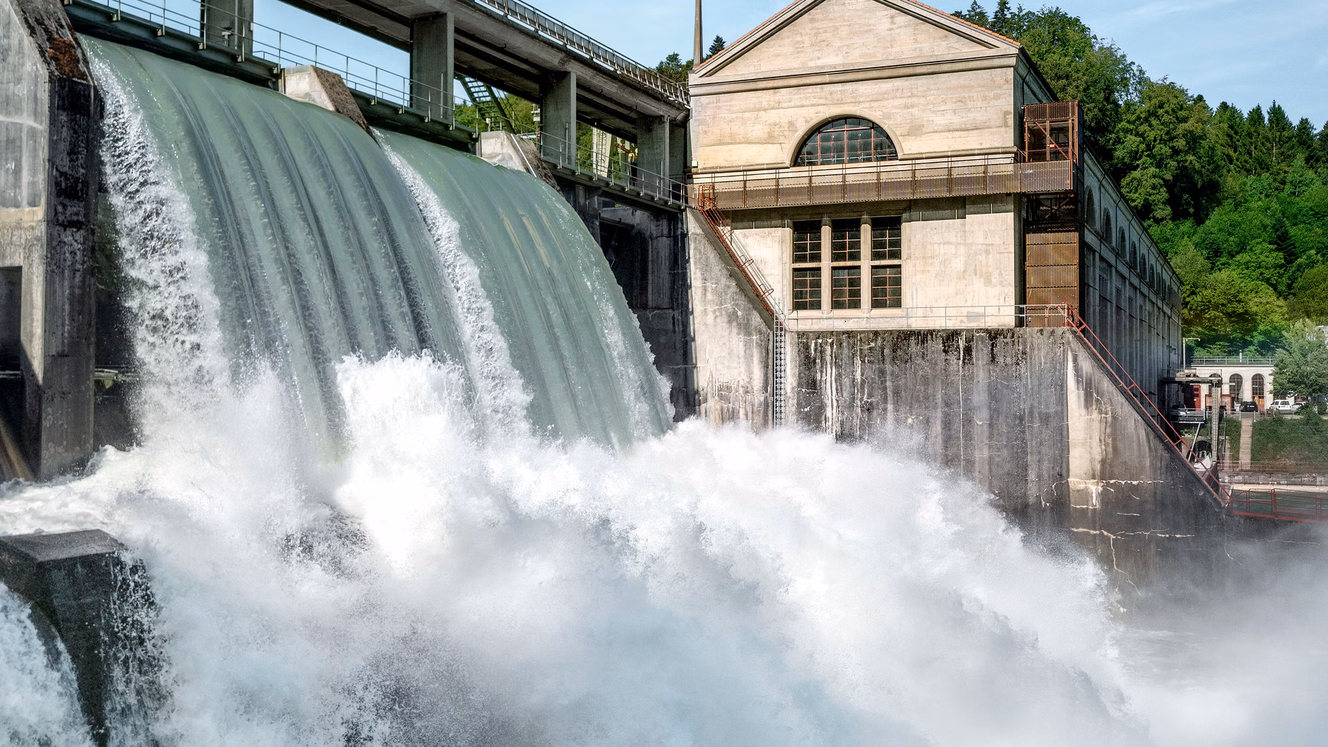 Wasserkraftwerk mit überströmendem Wehr und historischem Gebäude neben einer Brücke